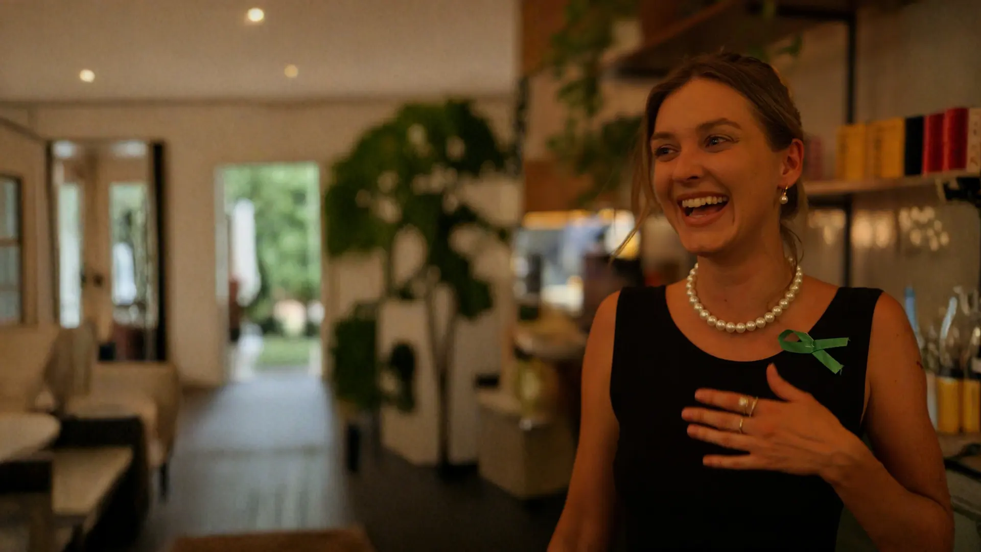 A guest wearing a pearl necklace and a green ribbon at a past event